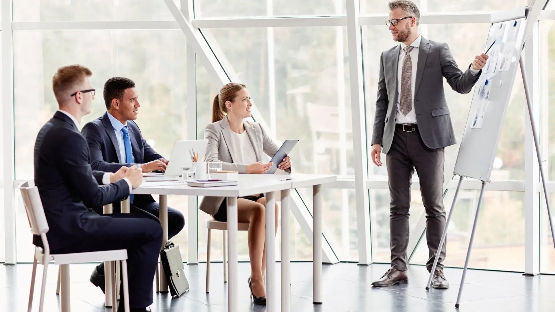 Four people dressed in corporate wear are having a training session. One of the four is presenting something on the whiteboard while the other three are listening to his discussion. 